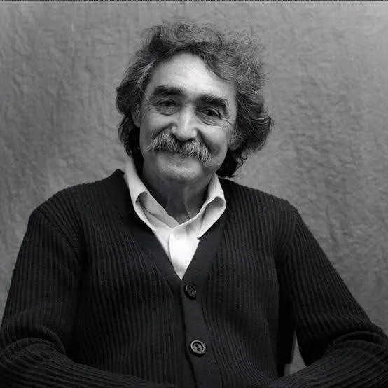 Retrato de Jesús Soto: hombre sonriente de pelo rizado canoso y bigote, con chaqueta de punto oscura y camisa blanca.